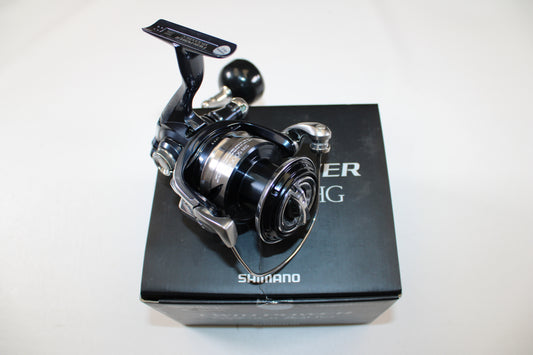 A Shimano Twinpower SW C TPSW5000HGC used spinning reel in mint condition sits atop its original black box packaging with white text, set against a plain white background.