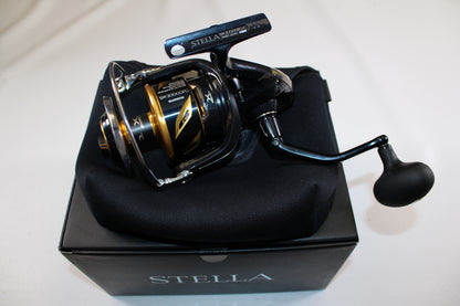A Shimano Stella SW C STLSW20000PGC spinning reel in mint condition sits on its padded case and "STELLA" box against a white background—ideal for anyone seeking quality used Shimano gear or looking to trade in a rod and reel for store credit.