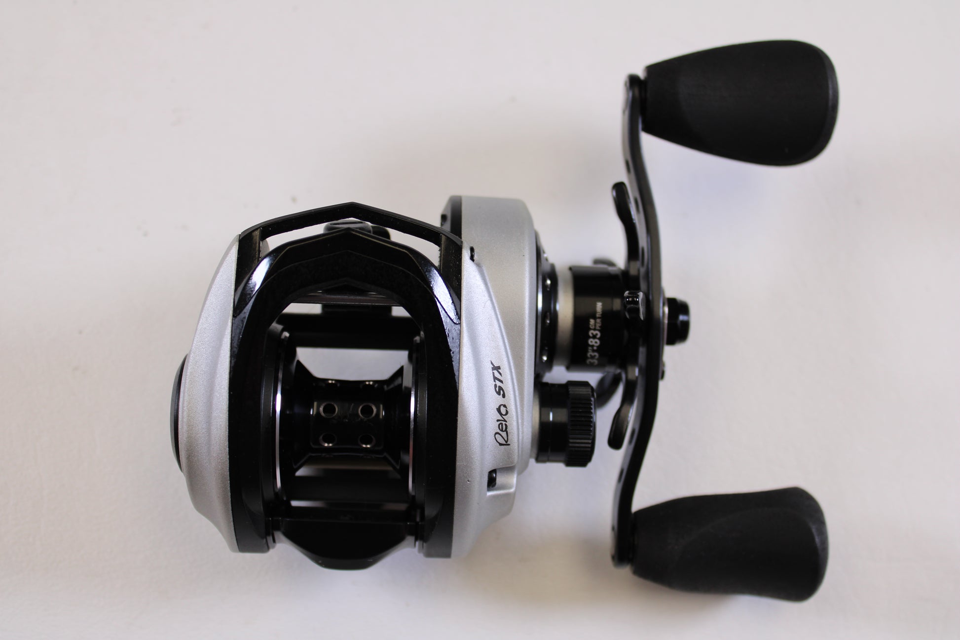 An Abu Garcia Revo STX Gen 4 REVO3STX-SHS 8.0:1 RH casting reel in excellent used condition, featuring a silver and black design with dual black handles, is ideal for our Rod and Reel Trade-In Program for store credit.