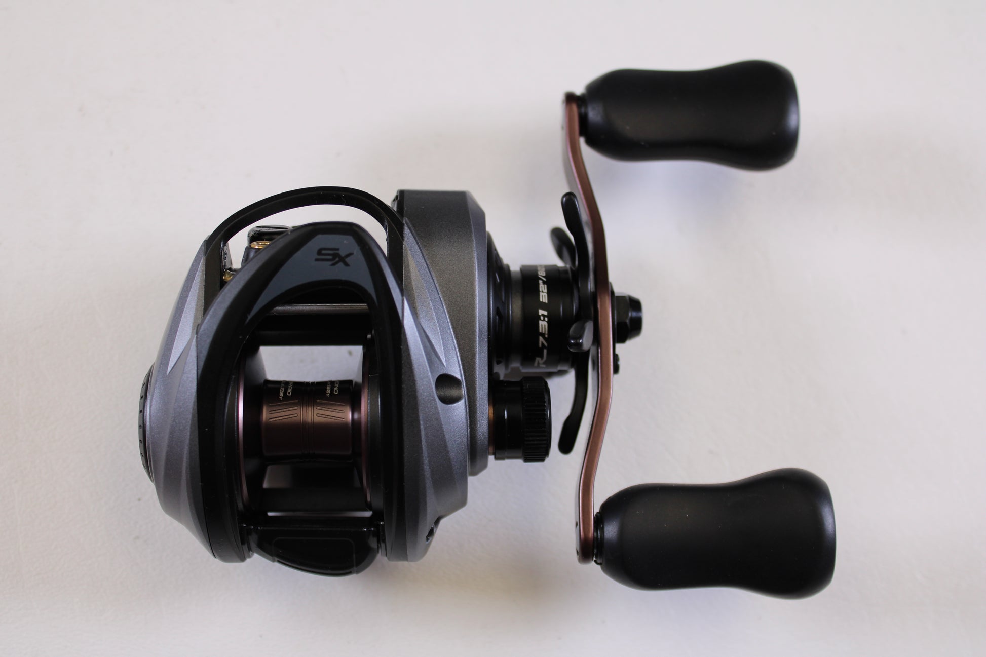 A close-up of an Abu Garcia Revo SX REVO5SXHSLP 7.3:1 RH used casting reel in excellent condition, featuring two black handle grips on a plain white background—ideal for those interested in used gear or a rod and reel trade-in for store credit.