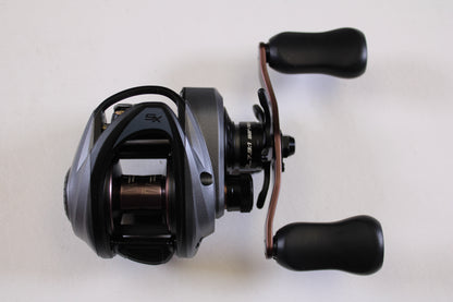 A close-up of an Abu Garcia Revo SX REVO5SXHSLP 7.3:1 RH used casting reel in excellent condition, featuring two black handle grips on a plain white background—ideal for those interested in used gear or a rod and reel trade-in for store credit.