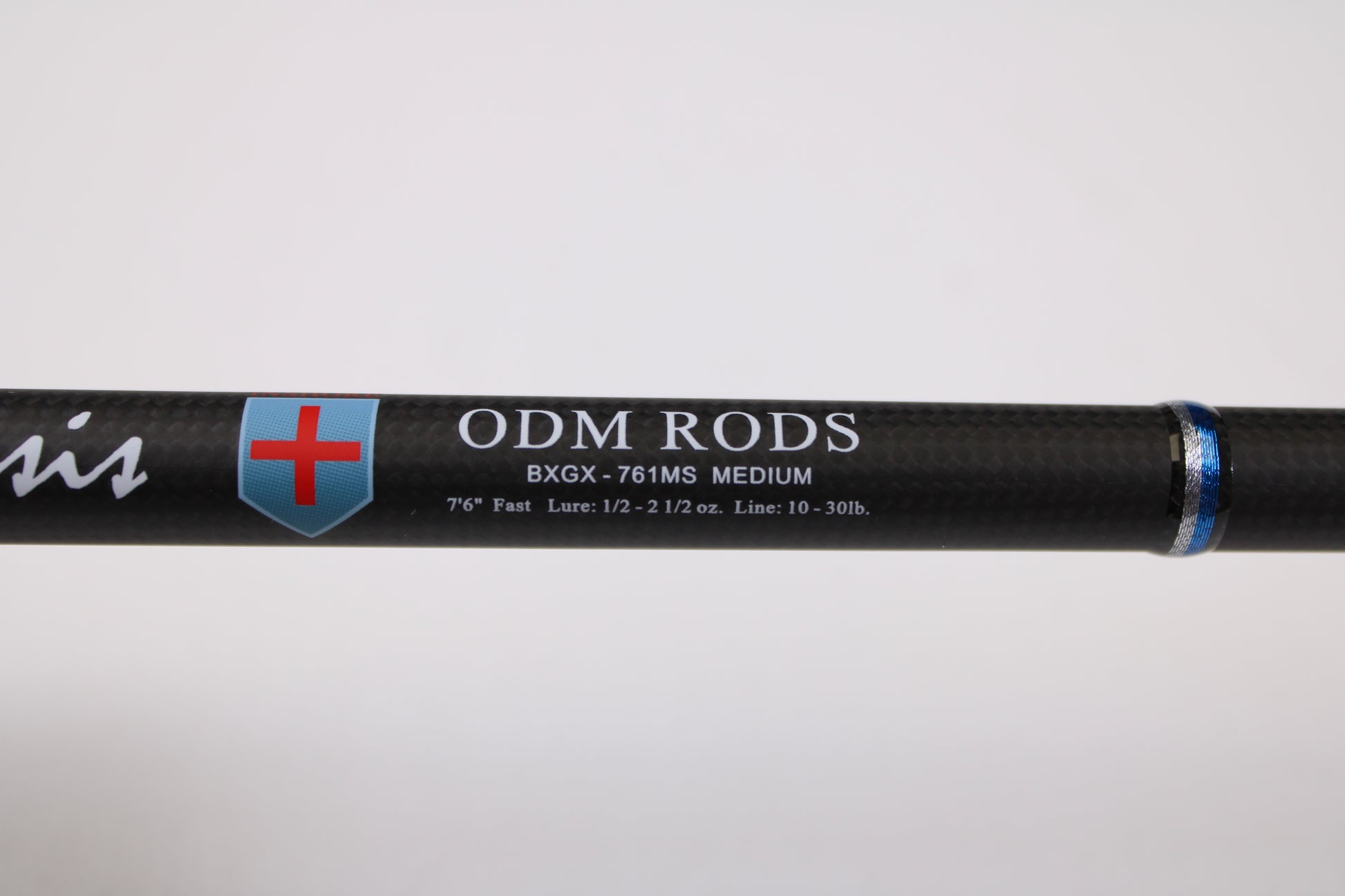 Close-up of an ODM Rods Genesis Inshore BXGX 761MS 7'6" Medium Used Spinning Rod in excellent condition, featuring a red and blue shield logo and specs in white—eligible for our rod and reel trade-in program for store credit.