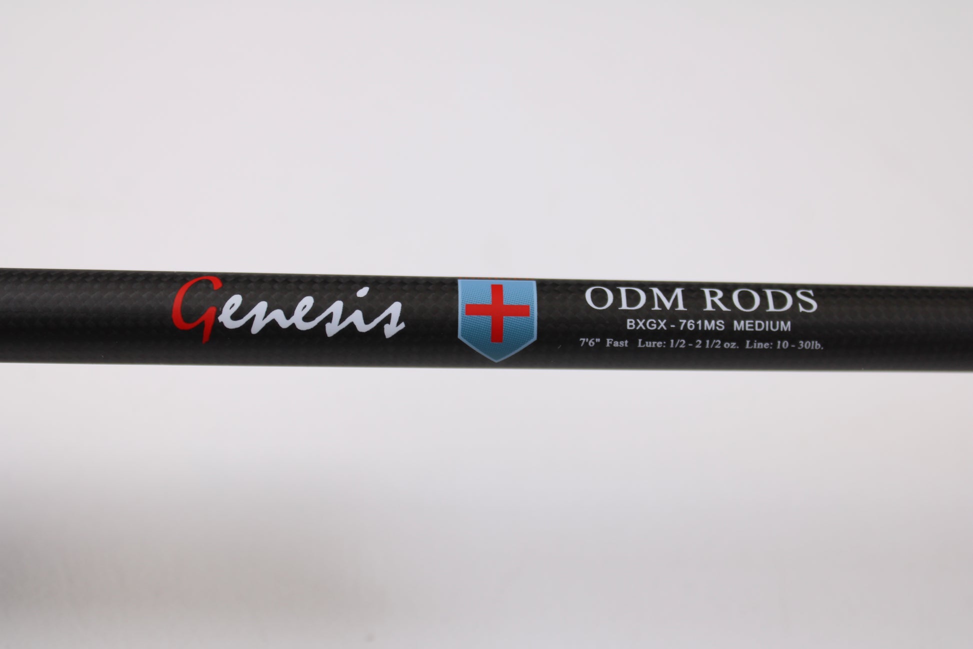 Close-up of an ODM Rods Genesis Inshore BXGX 761MS 7'6" Medium used spinning rod with blue and red shield logo. Specs: Fast action, 1/2–2 1/2 oz., line rating 10–30 lb. Ideal for anglers using our rod and reel trade-in program.