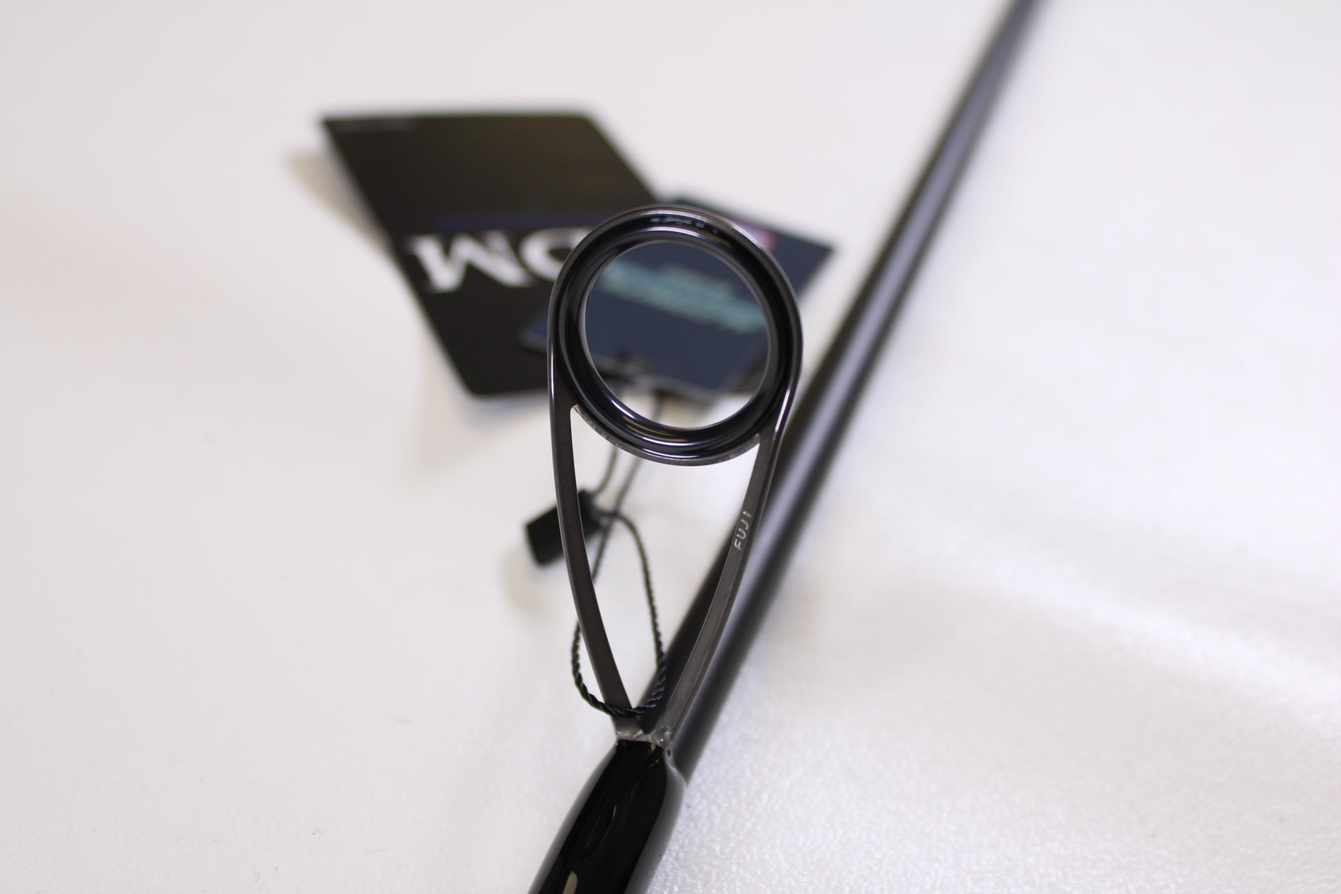 Close-up of an ODM Rods Genesis Inshore BXGX 761MS 7'6" Medium spinning rod guide ring, tags attached in the background—ideal for those looking to trade in or earn store credit on used fishing gear.