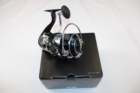 A Daiwa Certate SW G CERTATESWG18000-H used spinning reel in mint condition is shown upright, with its handle and spool visible, displayed on a black box against a white background. The box features text on the front edge. Brand: Daiwa.