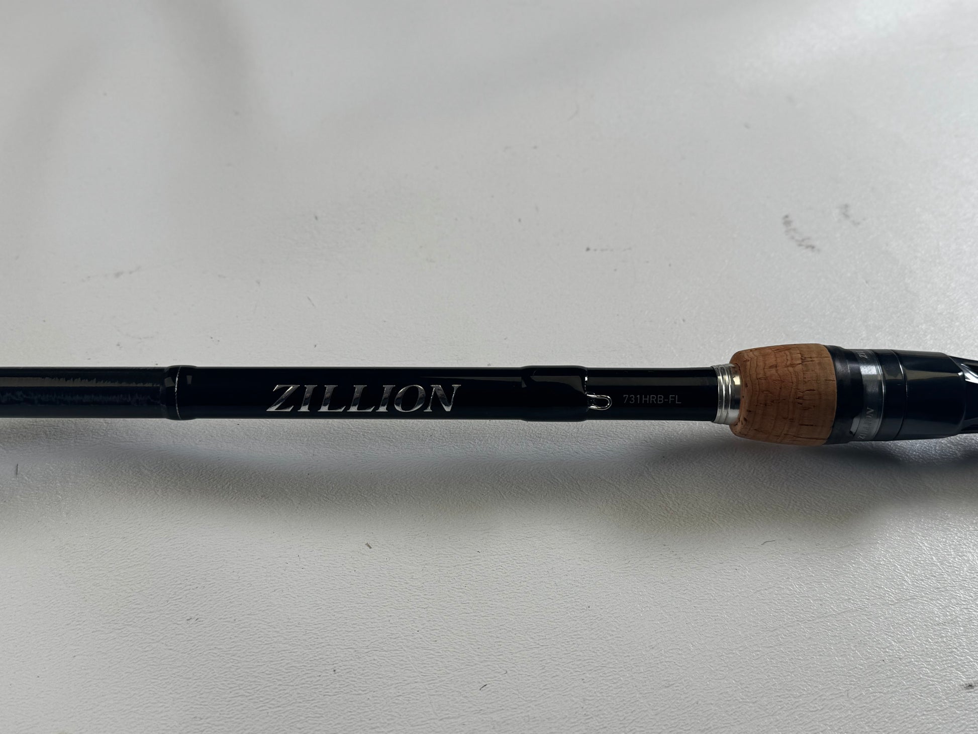 The Daiwa Zillion ZLON731HRB-FL 7'3" Heavy Casting Rod in excellent condition, with "Zillion" inscribed in silver and a cork handle, is featured in our Rod and Reel Trade-In Program on a white surface, offering store credit for upgrading your used gear.