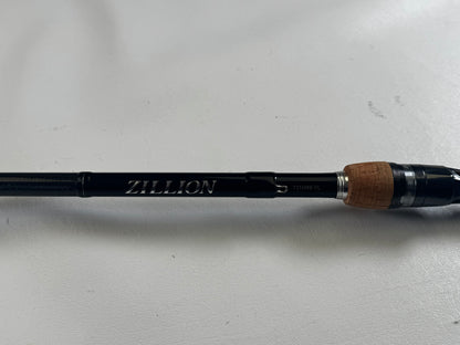 The Daiwa Zillion ZLON731HRB-FL 7'3" Heavy Casting Rod in excellent condition, with "Zillion" inscribed in silver and a cork handle, is featured in our Rod and Reel Trade-In Program on a white surface, offering store credit for upgrading your used gear.