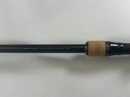 Close-up of a Daiwa BLX BLXSG7111XHXB Casting Rod showing text: "BLKSG714XHFB-7'11" XH LURE WT. 1/2-3oz LINE. 14-30lb." The cork and dark material handle is partly visible; the rod rests on a plain white surface. Excellent condition, used rod from Daiwa.