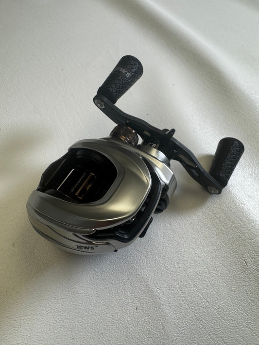 A Lew's HyperMag TLH1XHLG2 Casting Reel, featuring a silver and black design with dual textured handles, sits on a light gray surface. This used reel, in excellent condition, is ideal for upgrading through our Rod and Reel Trade-In program with valuable store credit options.