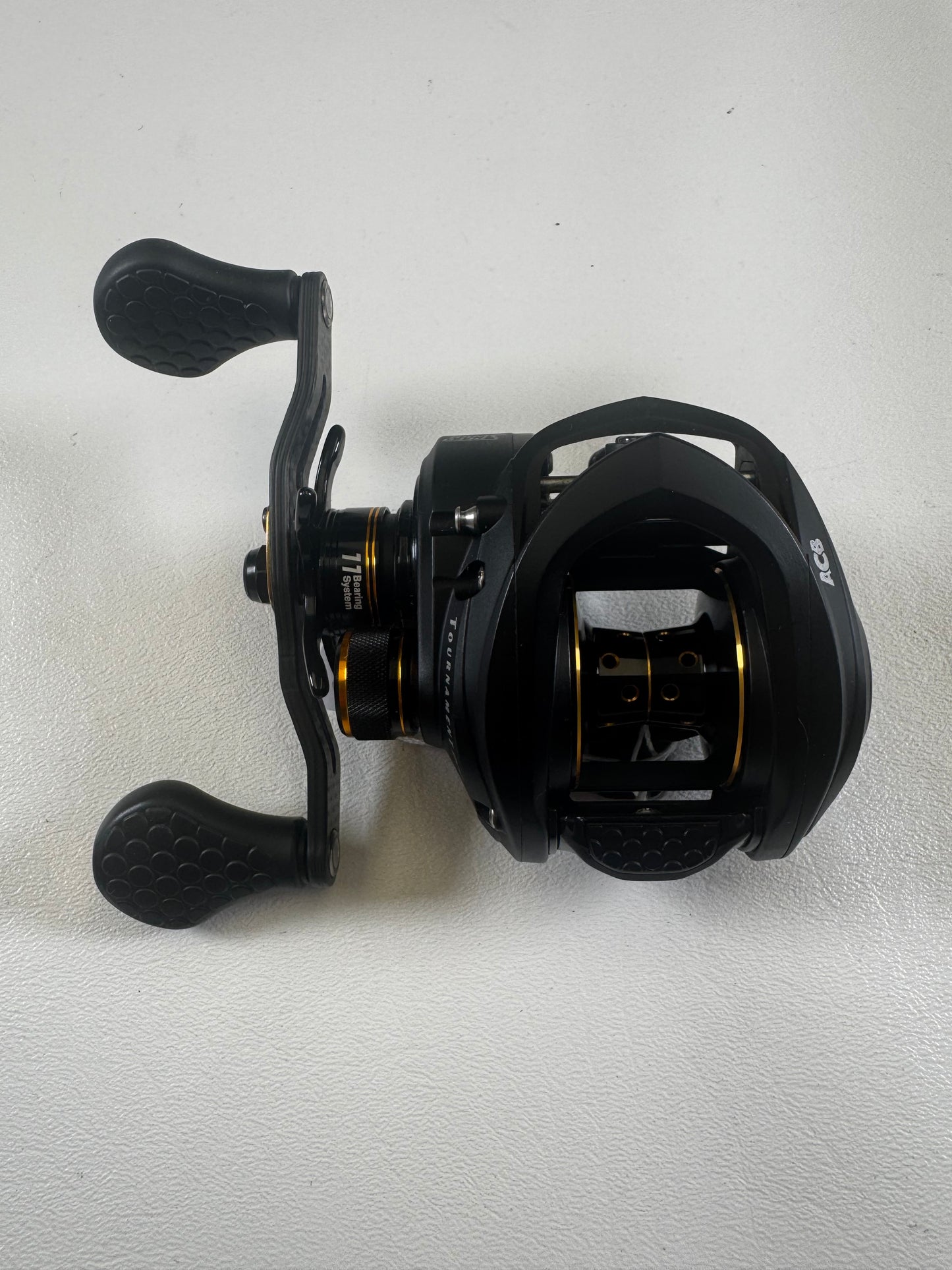 A Lew's Tournament Pro TP1SHLA 7.5:1 gear ratio baitcasting reel in excellent condition, with dual textured handles and gold accents, rests on a white surface—an ideal upgrade through our Rod and Reel Trade-In program.