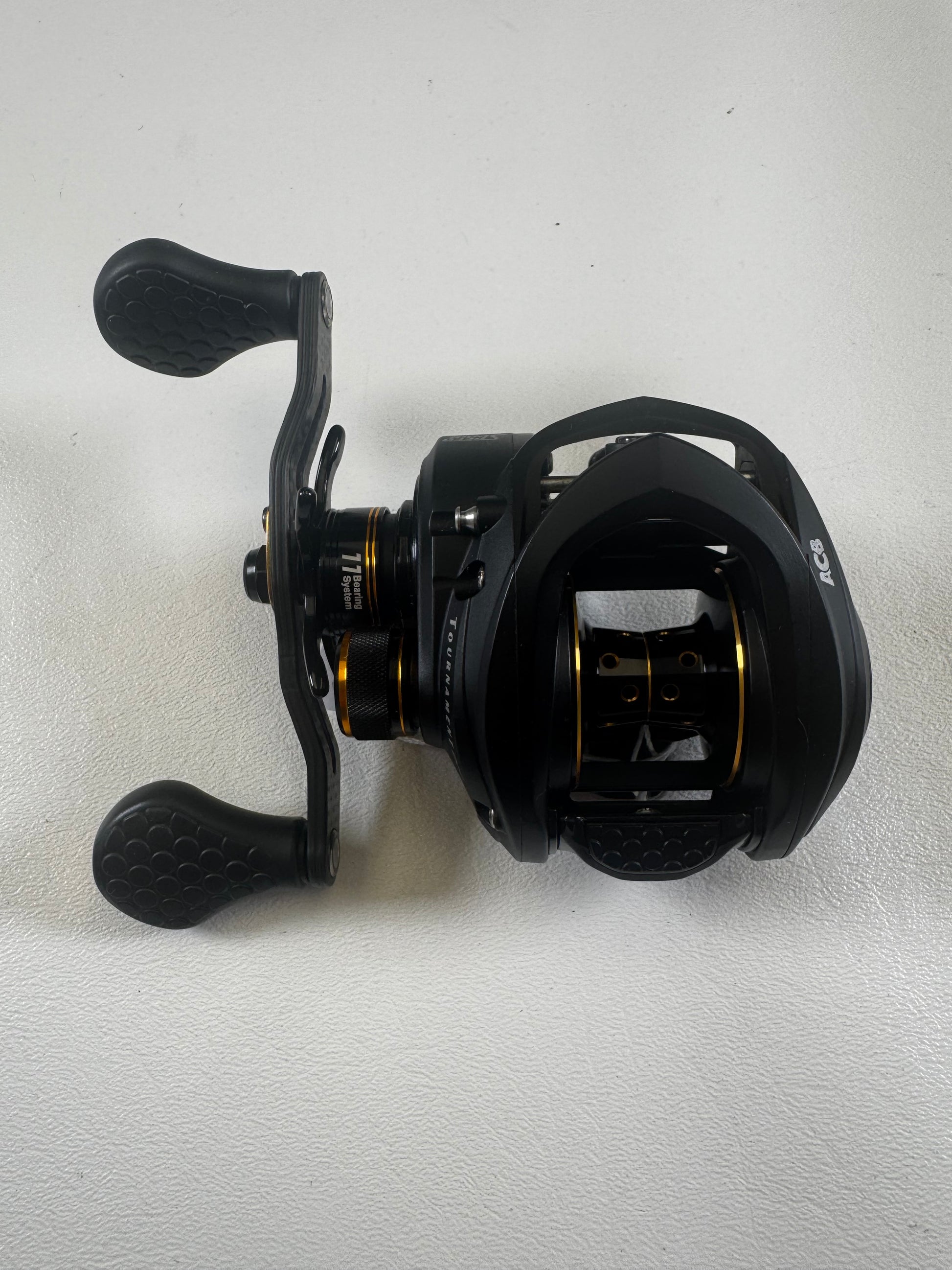 A Lew's Tournament Pro TP1SHLA 7.5:1 gear ratio baitcasting reel in excellent condition, with dual textured handles and gold accents, rests on a white surface—an ideal upgrade through our Rod and Reel Trade-In program.