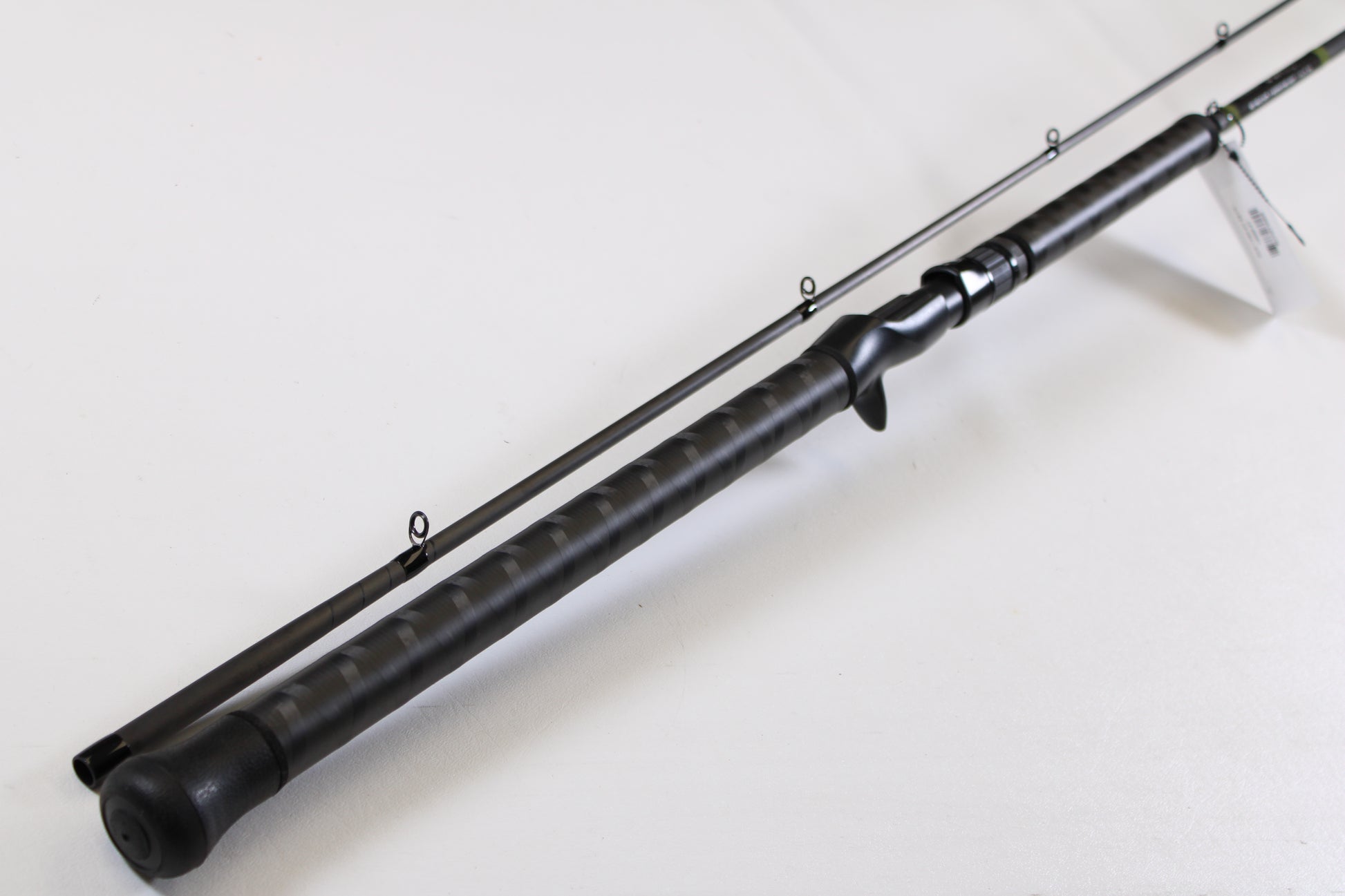 A close-up of the G. Loomis GCX Salmon 1083-2C SATR 9'0" Medium Heavy 2 Piece Used Casting Rod in mint condition, displayed diagonally to highlight its multiple guide rings and textured handle, from our rod and reel trade-in program.