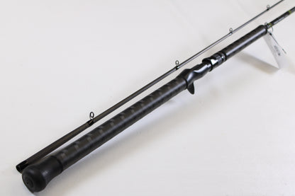 A close-up of the G. Loomis GCX Salmon 1083-2C SATR 9'0" Medium Heavy 2 Piece Used Casting Rod in mint condition, displayed diagonally to highlight its multiple guide rings and textured handle, from our rod and reel trade-in program.