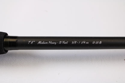 A close-up of the 13 Fishing Muse 7'6" Medium Heavy Used Casting Rod in excellent condition shows white specs: "7'6" Medium Heavy - X-Fast 3/8 - 1 1/4 oz 12-25 lb," ideal for our rod and reel trade-in program, against a light background.