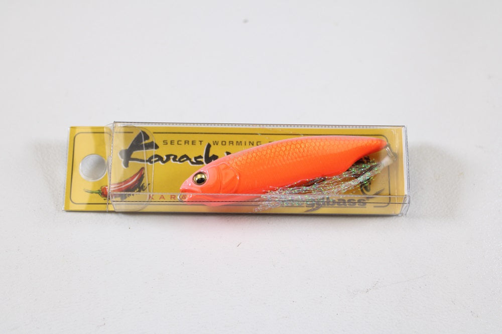 The Megabass Karashi (SP-C) Secret V-Ore is a bright orange, fish-shaped finesse soft bait with a shiny tail, packaged in a clear case—an ideal addition to any Megabass collection.