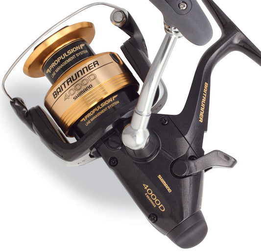 A close-up of the Shimano Baitrunner BTR4000D Spinning Fishing Reel shows gold and black details, visible Shimano branding, and spool and handle parts, highlighting its advanced Propulsion Line Management System.