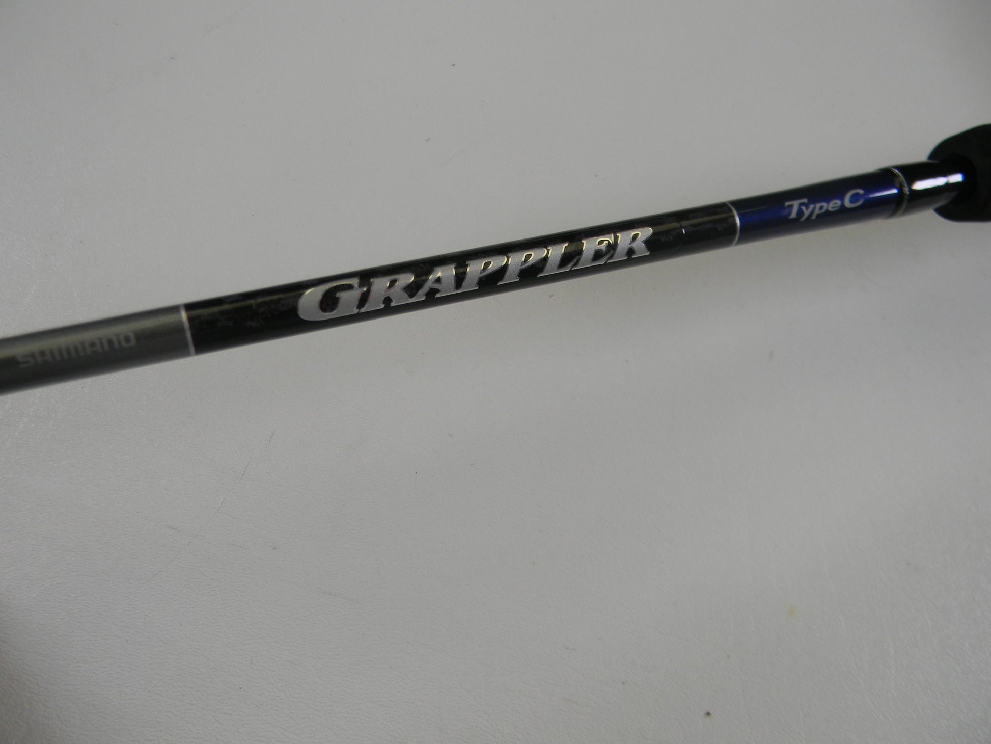 A close-up of the Shimano Grappler Type C GRPCS70L 7'0" Light Used Spinning Rod in excellent condition, featuring "GRAPPLER" in bold silver letters—ideal for those looking to upgrade with our Rod and Reel Trade-In Program.