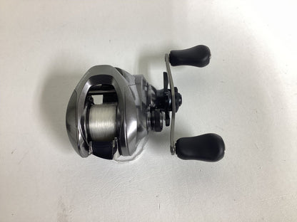 A Shimano Chronarch MGL CHMGL150HG casting reel in excellent condition, featuring a silver body with black handles and white fishing line, is displayed on a plain white surface.