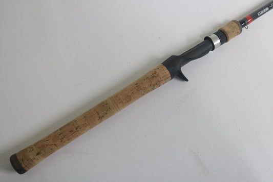 The G. Loomis GCX 843C MBR Used Casting Rod features a cork grip handle, a reel seat, and a black attachment area. It's displayed on a plain white background and is in excellent condition.