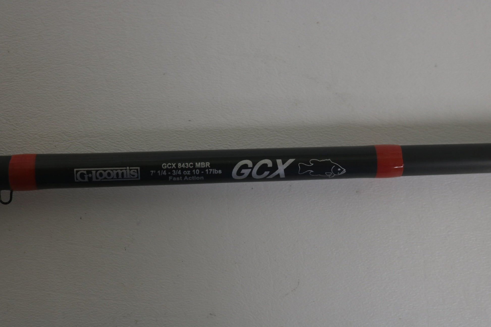 Close-up of a G. Loomis GCX 843C MBR rod in black with red accents, labeled "7'1," 3/16-5/8 oz, 10-17 lbs," and "Fast Action," featuring a fish icon.