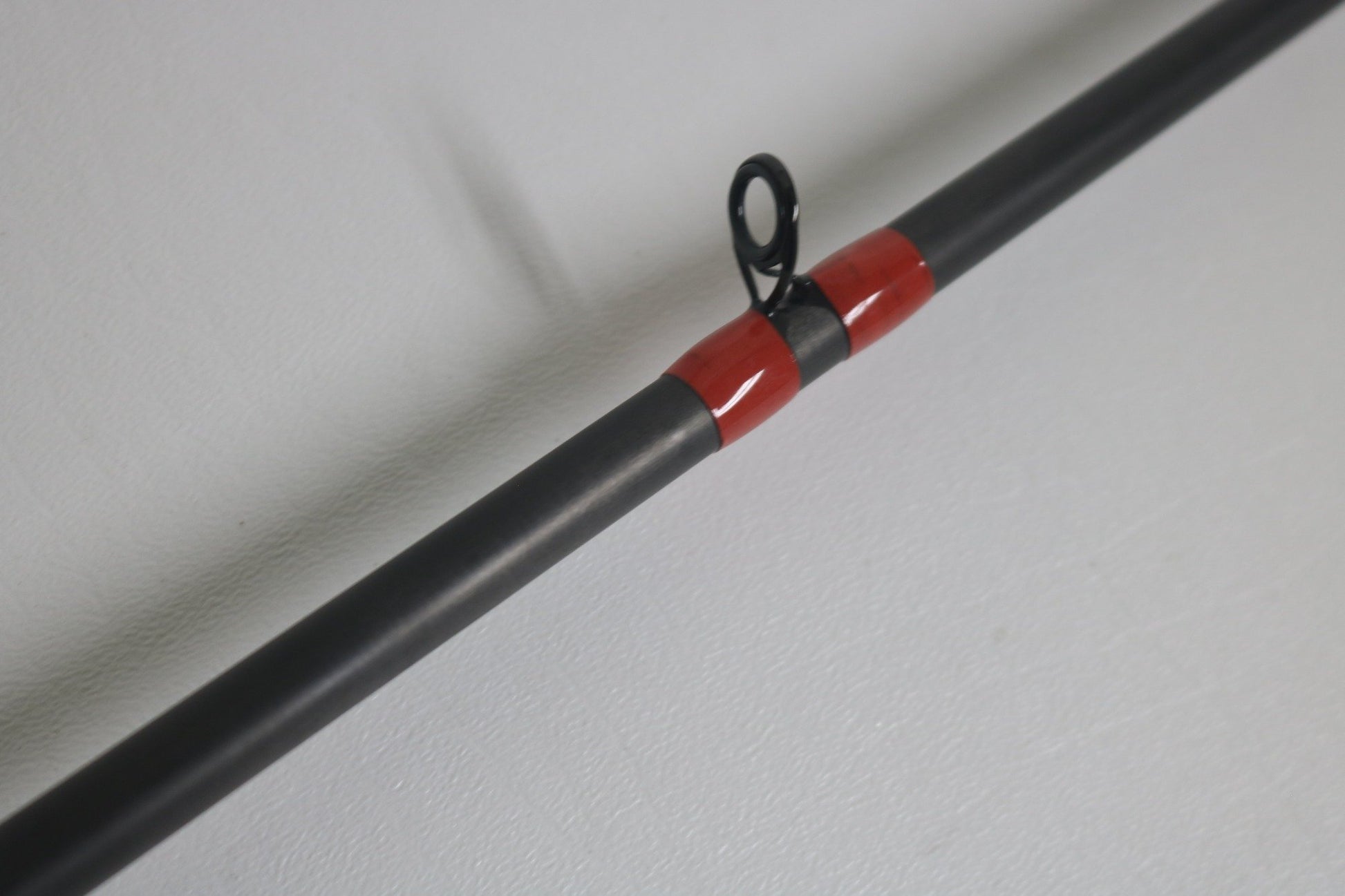 Close-up of the G. Loomis GCX 843C MBR Used Casting Rod in excellent condition, featuring a red wrapping near the guide ring, on a light gray surface.