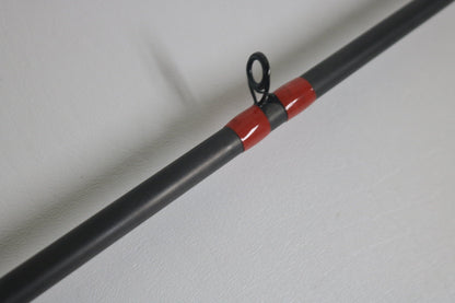 Close-up of the G. Loomis GCX 843C MBR Used Casting Rod in excellent condition, featuring a red wrapping near the guide ring, on a light gray surface.
