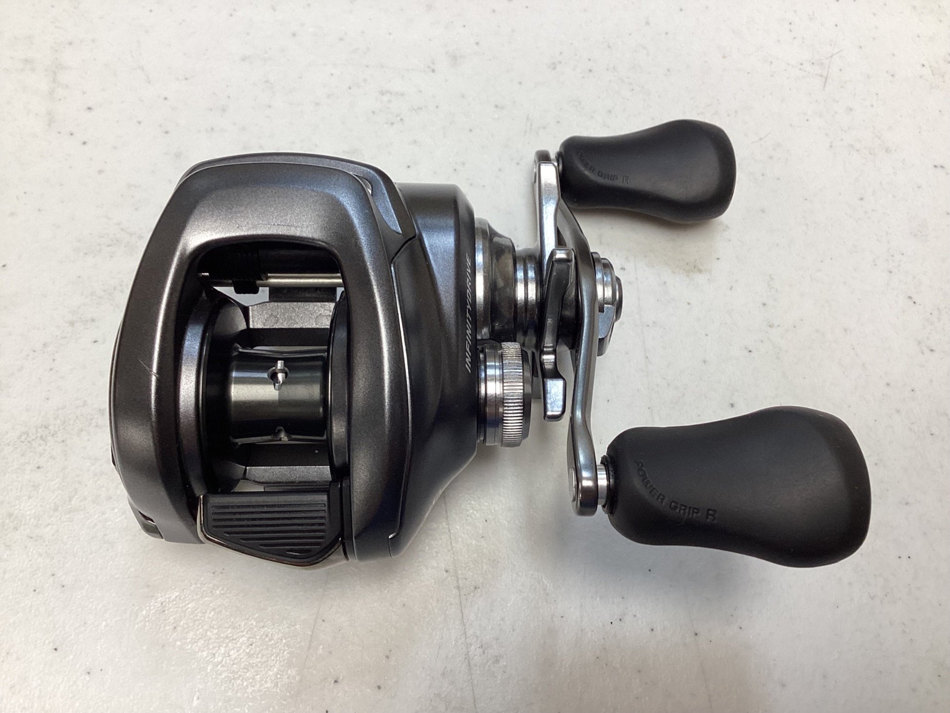 A close-up of a Shimano Bantam 150XG 8.1:1 baitcasting reel with two rubber handles, shown on a light surface. The used Shimano reel is in excellent condition, highlighting its spool and handle mechanism.