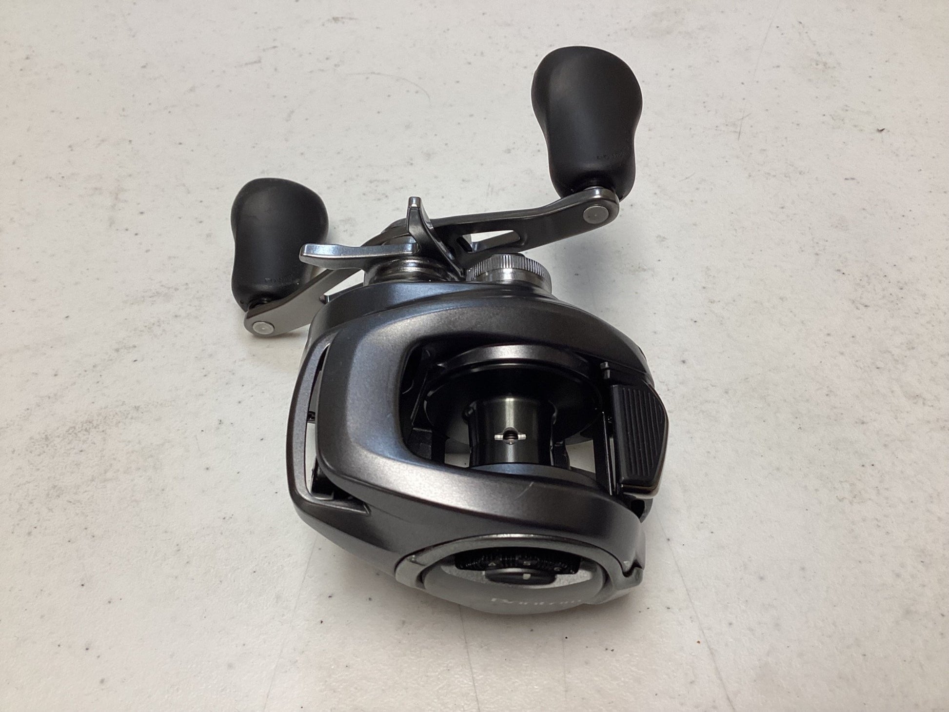 A close-up of a Shimano Bantam 150XG 8.1:1 baitcasting reel in excellent used condition with dual handles, shown on a white textured surface.