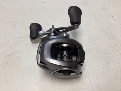 A close-up of a Shimano Bantam 150XG 8.1:1 baitcasting reel in excellent used condition with dual handles, shown on a white textured surface.