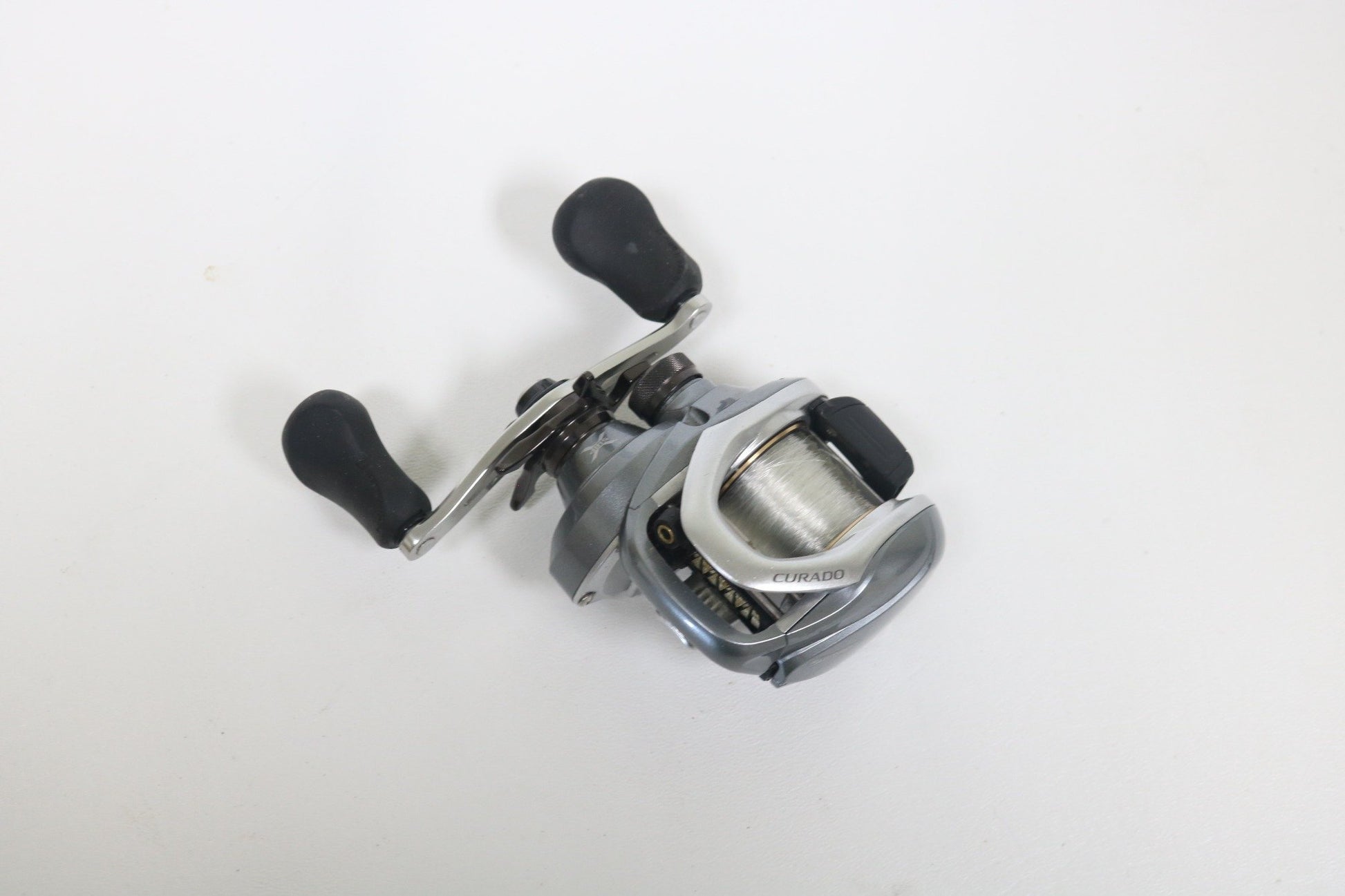 A Shimano Curado I 200PG 5.5:1 Used Casting Reel in excellent condition, featuring a silver and black design with two black handles, is displayed on a plain white surface—ideal for anglers exploring Used Gear or our Rod and Reel Trade-In.
