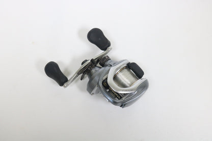 A Shimano Curado I 200PG 5.5:1 Used Casting Reel in excellent condition, featuring a silver and black design with two black handles, is displayed on a plain white surface—ideal for anglers exploring Used Gear or our Rod and Reel Trade-In.