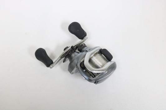 A Shimano Curado I 200PG 5.5:1 Used Casting Reel in excellent condition, featuring a silver and black design with two black handles, is displayed on a plain white surface—ideal for anglers exploring Used Gear or our Rod and Reel Trade-In.