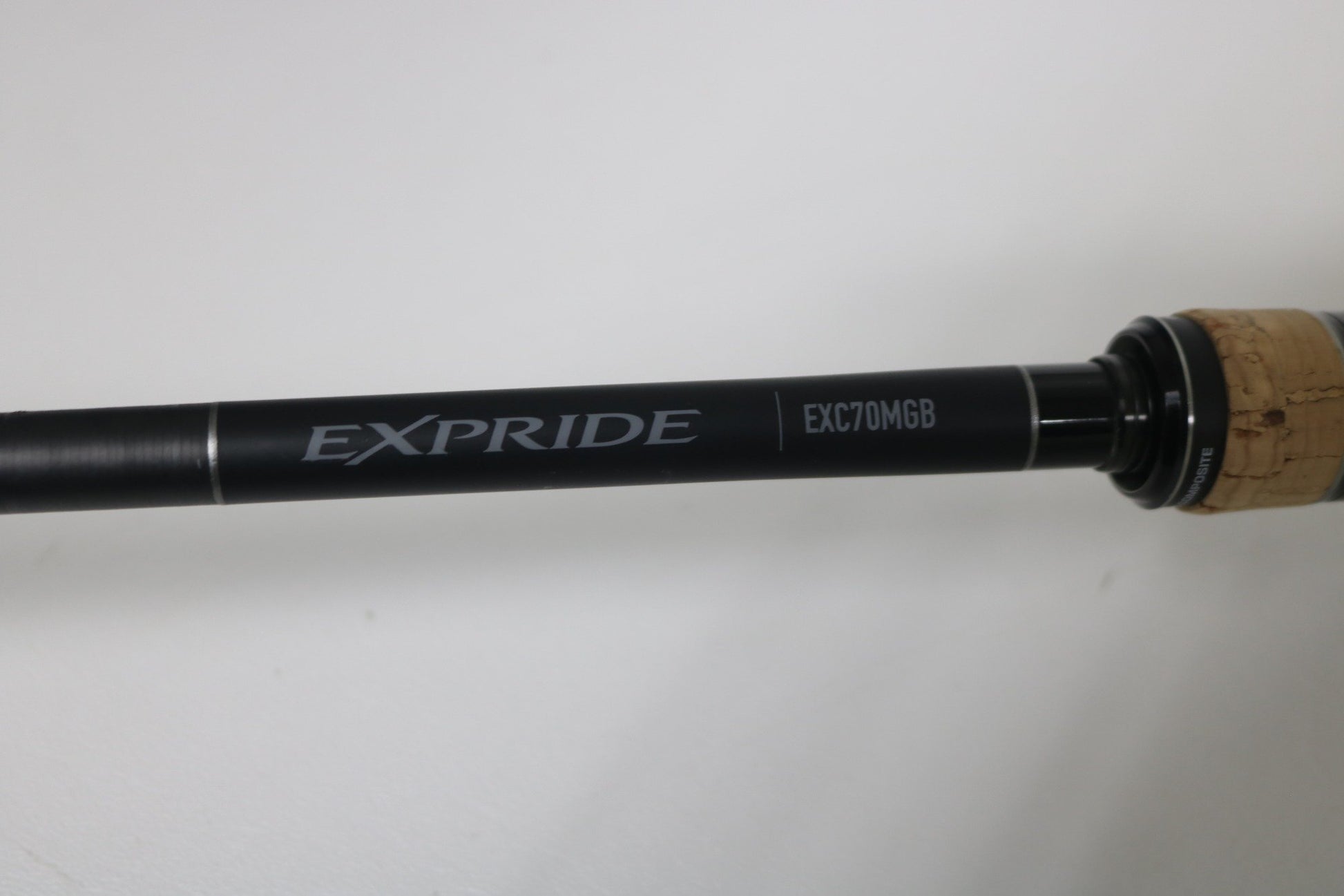 A close-up of the Shimano Expride B EXC70MGB Used Casting Rod in excellent condition, featuring a cork handle and black finish, set against a plain white background.