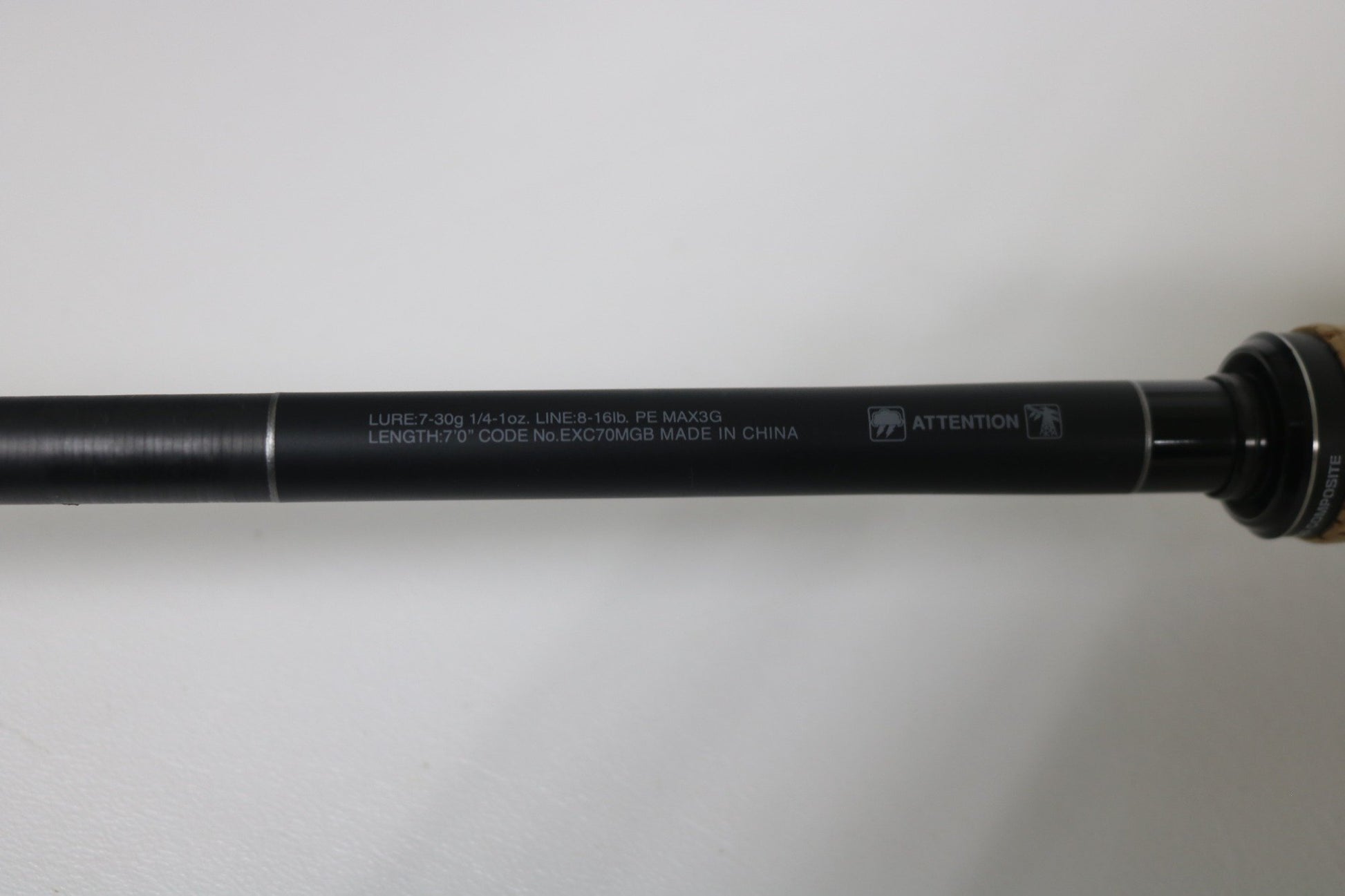 A close-up of a Shimano Expride B EXC70MGB Used Casting Rod in excellent condition, showing white specs like lure weight, line rating, length, code, and "Made in China," with part of the wooden handle on the right.