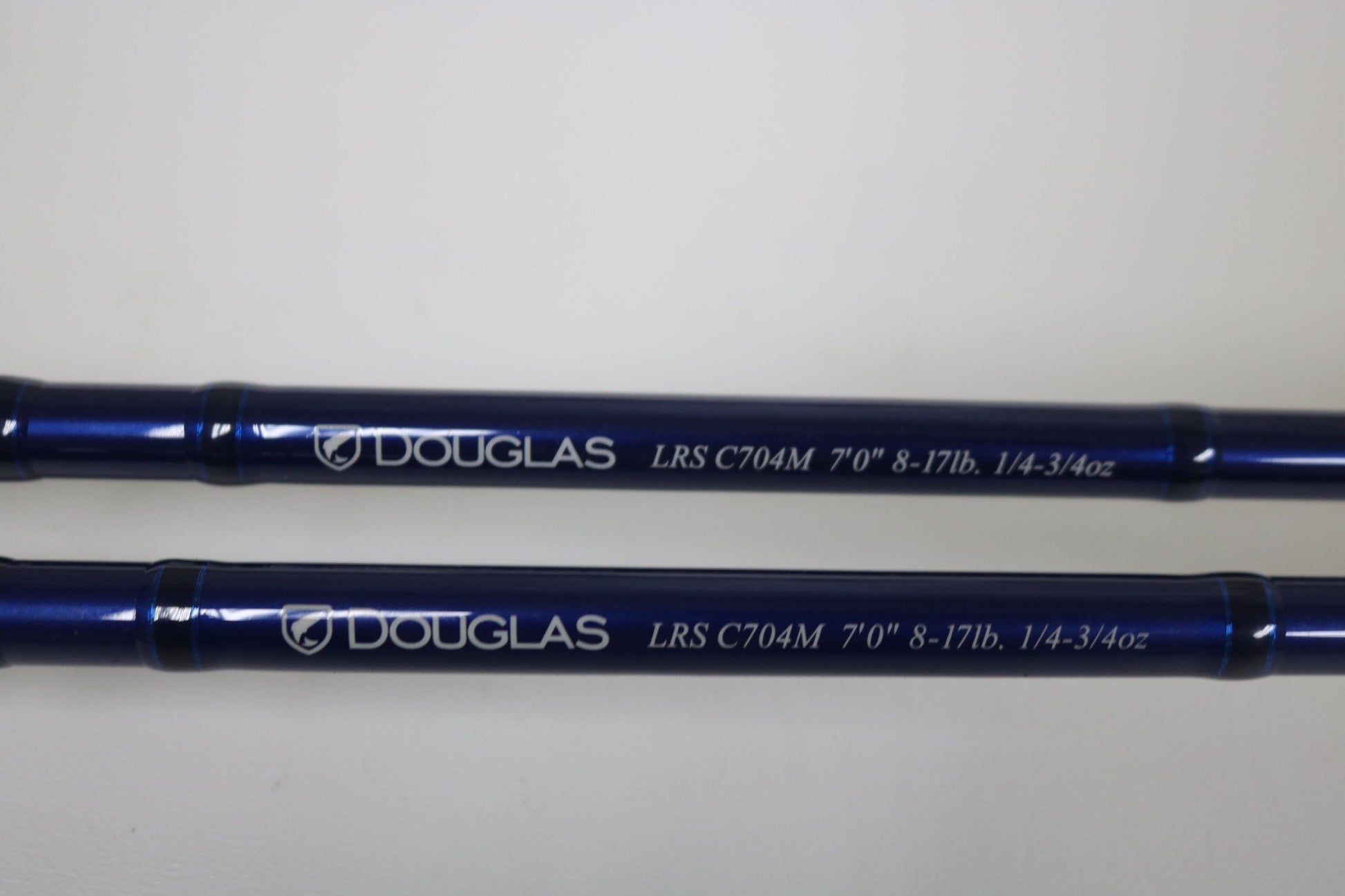 Two blue Douglas LRS C704M Casting Rods in very good used condition, each with white "DOUGLAS LRS C704M 7'0" 8-17lb. 1/4-3/4oz" text, ideal for anglers upgrading through our Trade-In or looking for quality pre-owned gear. Shown on a white background.