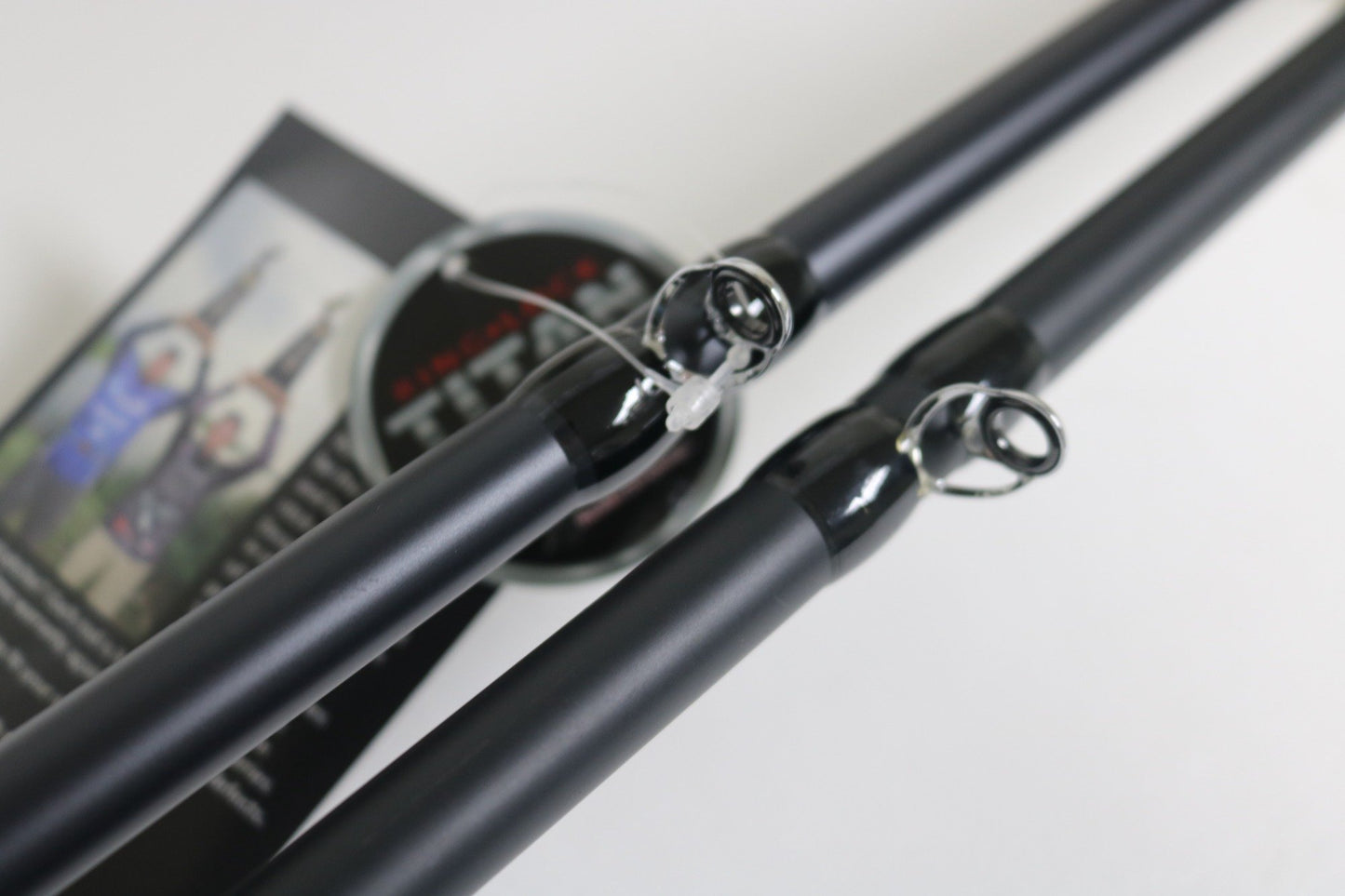 Close-up of two Fitzgerald Titan HD THD76H and THD76XH Casting Rods (Used - Very Good Condition) side by side on a white surface, with a fishing-themed brochure in the background—great for those considering used gear or trade-ins.