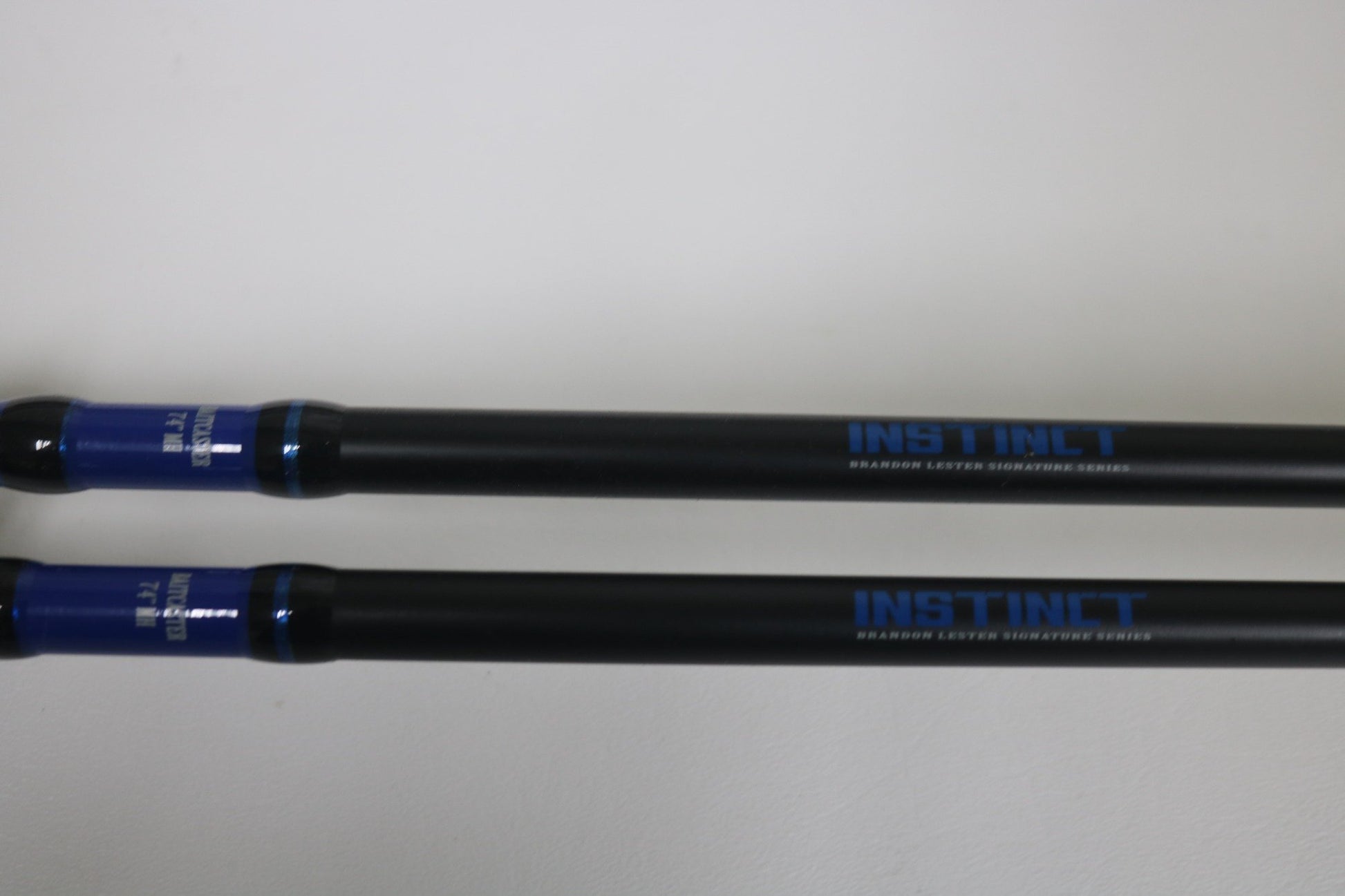 Two Mustad BLF Instinct 7'4" Medium Heavy Casting Rods in very good used condition lie parallel on a white surface. Trade in your used gear through our Nation's Best Rod and Reel Trade-In Program for store credit.