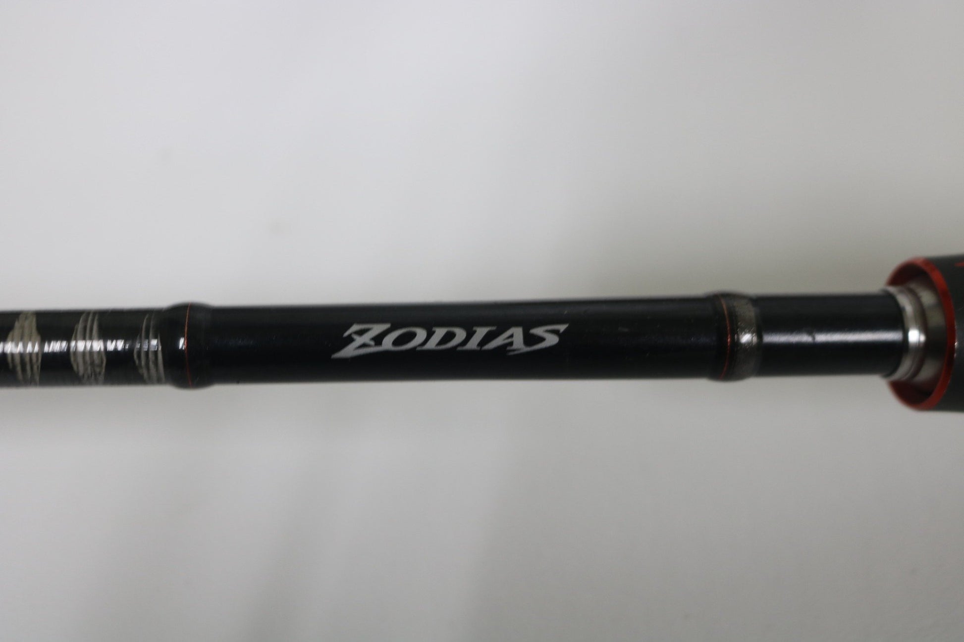 A close-up of a Shimano Zodias ZDC610MA 6'10" Medium used casting rod in very good condition, with "ZODIAS" in white on its black side. Ideal for Rod and Reel Trade-In Program or those shopping used Shimano gear. Light, plain background.