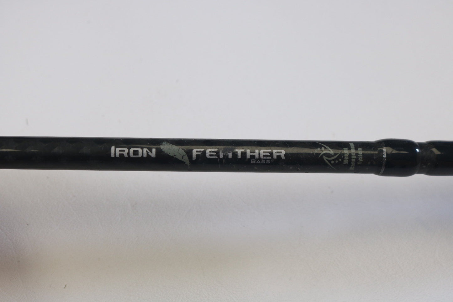 A close-up of a Waft Iron Feather 7'0" Medium Heavy Used Casting Rod in good condition—ideal for anglers seeking quality used gear or considering our Rod and Reel Trade-In for store credit. "IRON FEATHER BASS" is printed in white with a feather graphic on the rod.