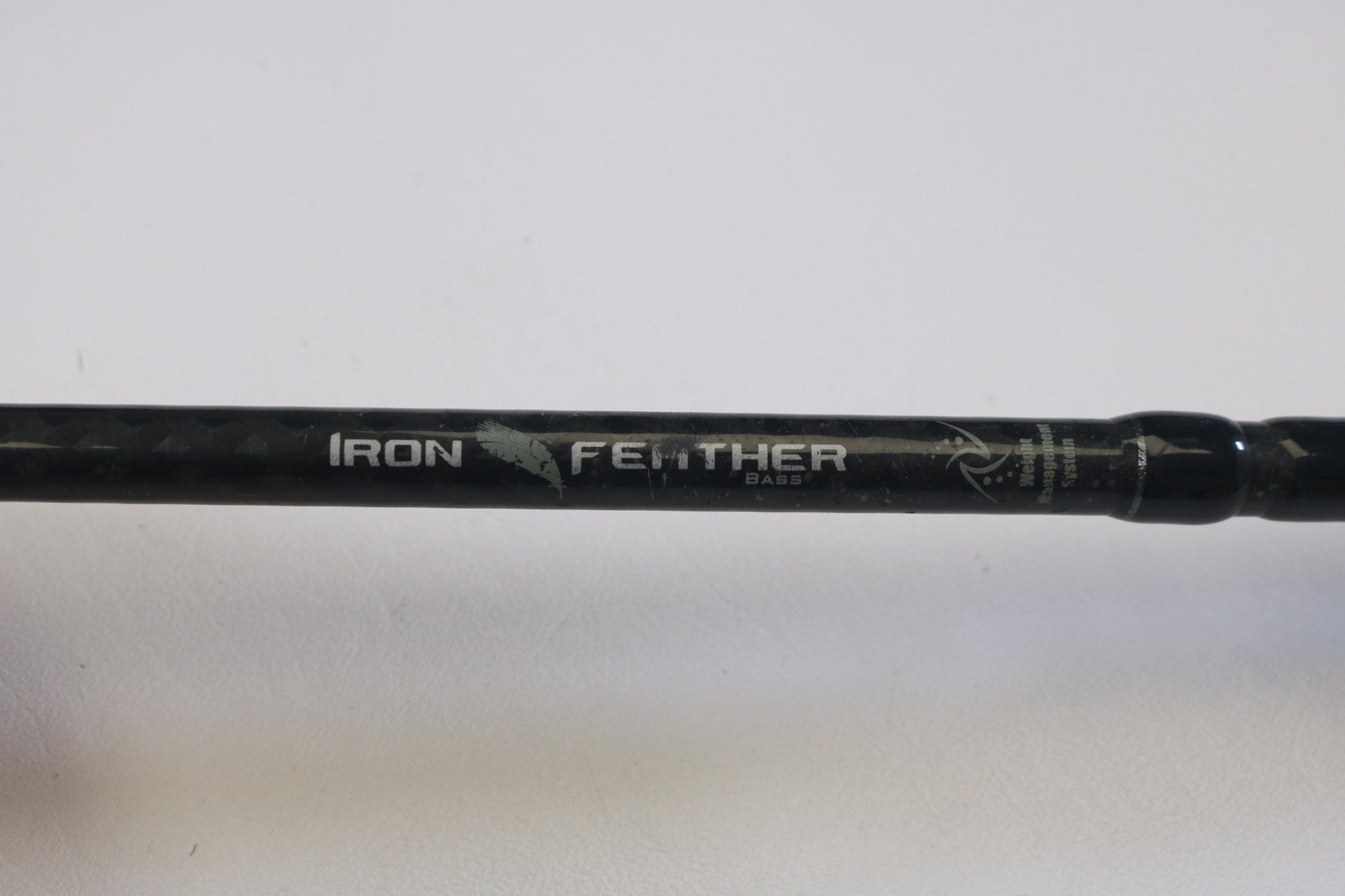 A close-up of a Waft Iron Feather 7'0" Medium Heavy Used Casting Rod in good condition—ideal for anglers seeking quality used gear or considering our Rod and Reel Trade-In for store credit. "IRON FEATHER BASS" is printed in white with a feather graphic on the rod.