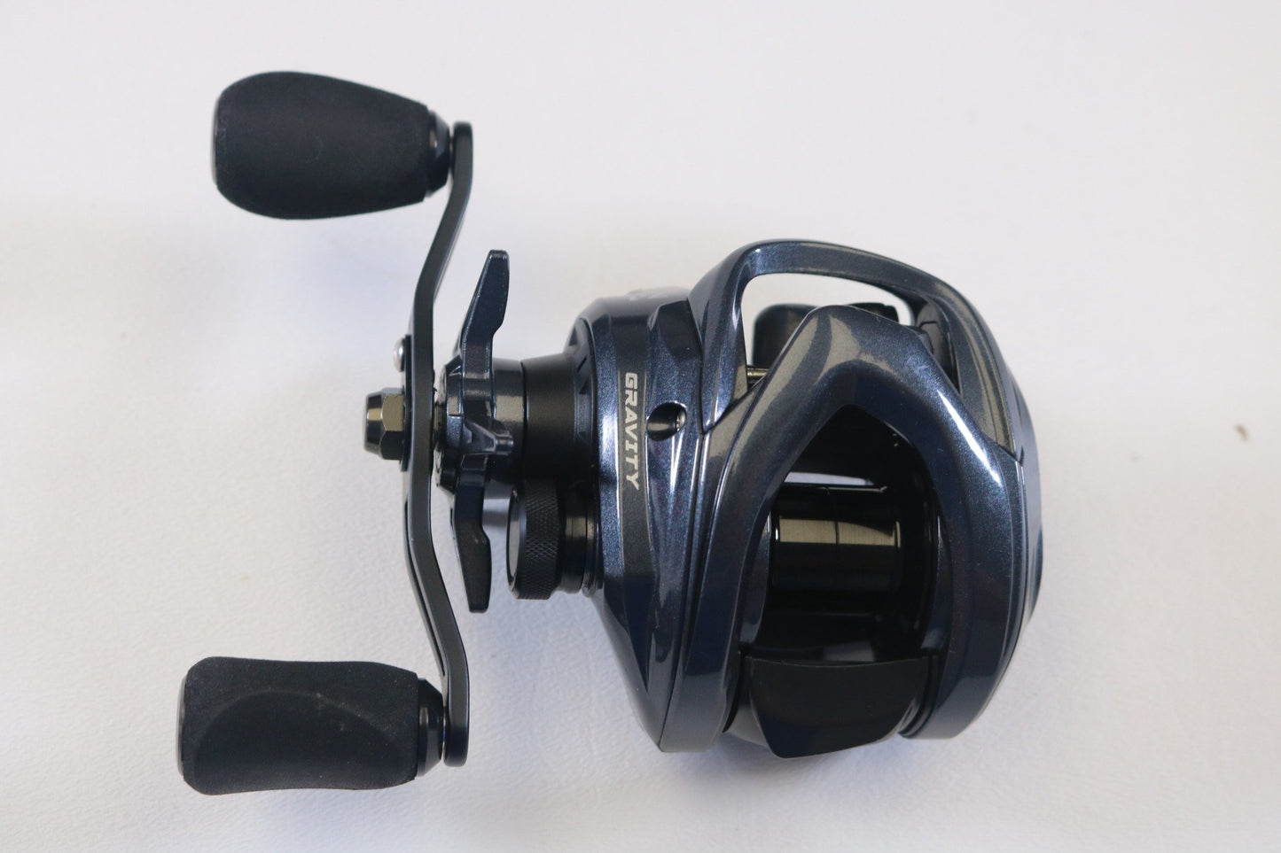 A close-up photo of an Ark Fishing Gravity 3 G3107L 7.1:1 LH Used Casting Reel in excellent condition, dark blue with black handles—ideal for those seeking quality pre-owned gear or eyeing a rod and reel trade-in for store credit.