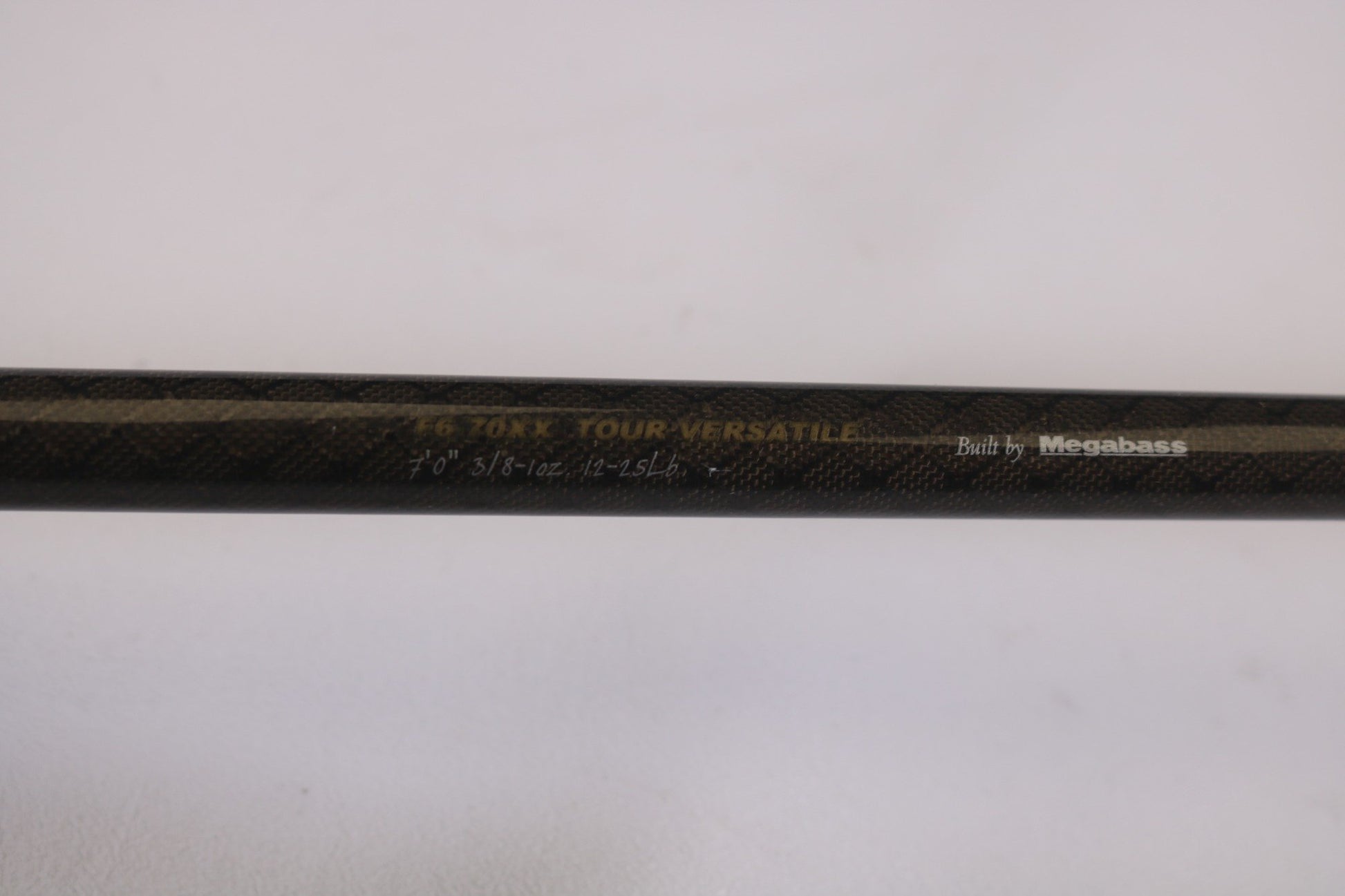 A close-up of the Megabass Orochi XX F6-70XX Tour Versatile 7'0" Heavy rod with "Built by Megabass" etched on its textured dark surface. Ideal for our Rod and Reel Trade-In Program, offering store credit for well-maintained used gear.