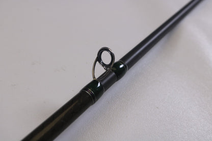 A close-up of the line guide on a Megabass Orochi XX F6-70XX 7'0" Heavy casting rod, part of our Rod and Reel Trade-In Program. The circular guide has a shiny metal finish, and the sleek dark rod rests on a light surface—perfect for assessing used gear conditions.