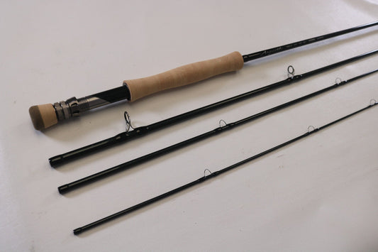 The G. Loomis Asquith ASQ 990-4 Used Fly Rod by G. Loomis is shown disassembled on a white surface, with its four sections, cork handle, rod guides, and metal reel seat aligned side by side in mint condition.