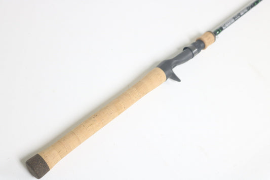 The G. Loomis IMX-Pro 843C CBR Used Casting Rod, partly visible and highlighting the cork handle and grey reel seat, lies diagonally on a white background.
