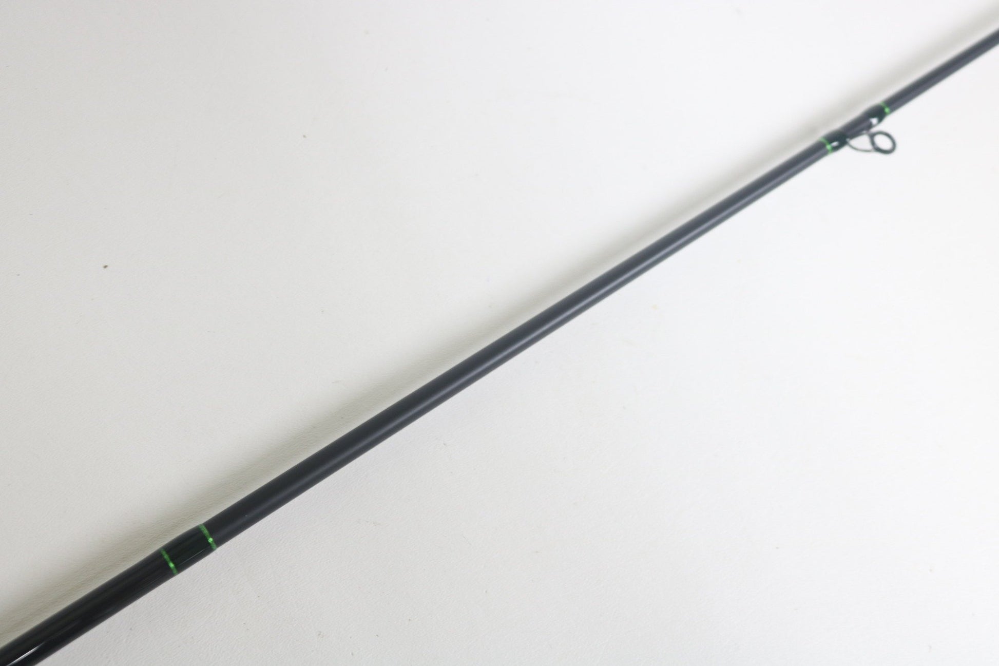 Close-up of a slender, dark G. Loomis IMX-Pro 843C CBR Casting Rod in excellent condition against a plain white background, featuring minimal green detailing near the guide rings.