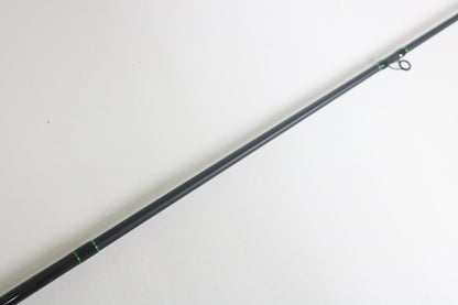 Close-up of a slender, dark G. Loomis IMX-Pro 843C CBR Casting Rod in excellent condition against a plain white background, featuring minimal green detailing near the guide rings.